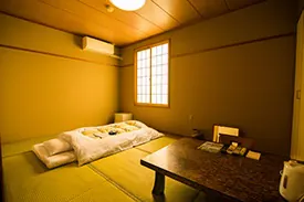 和室8畳。畳敷きに布団を1組敷き、座卓と障子窓のある客室